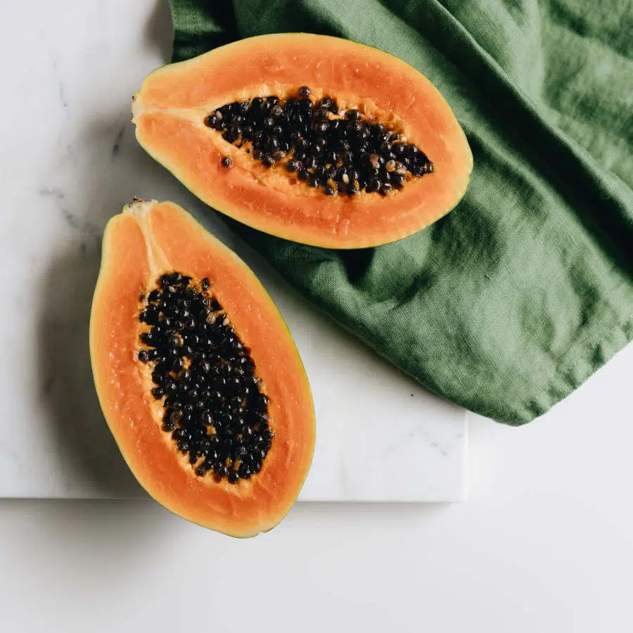 Eine halbierte Papaya liegt auf einem Marmorbrett. Unter einer der Hälften liegt ein grünes Tuch.