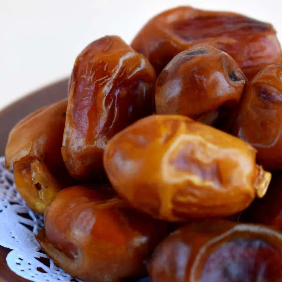 Auf einem kleinen braunen Teller liegen mehrere Datteln aufeinander.