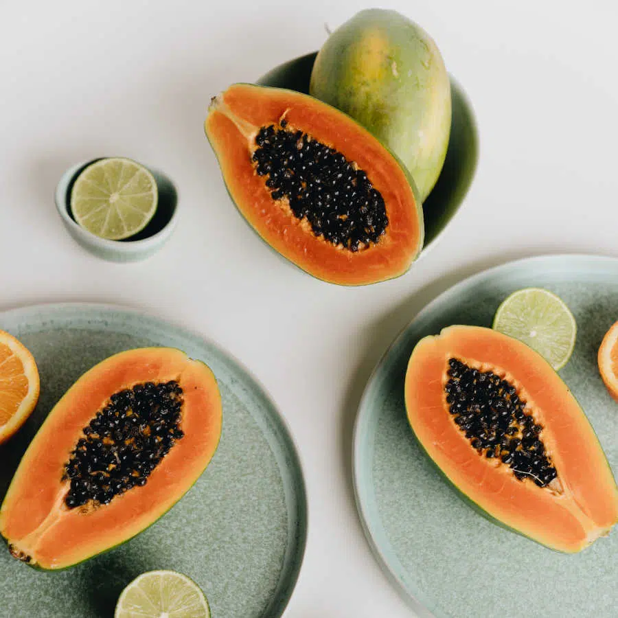 Drei aufgeschnittene Papayahälften liegen mit aufgeschnittenen Zitrusfrüchten auf pastellgrünen Tellern.