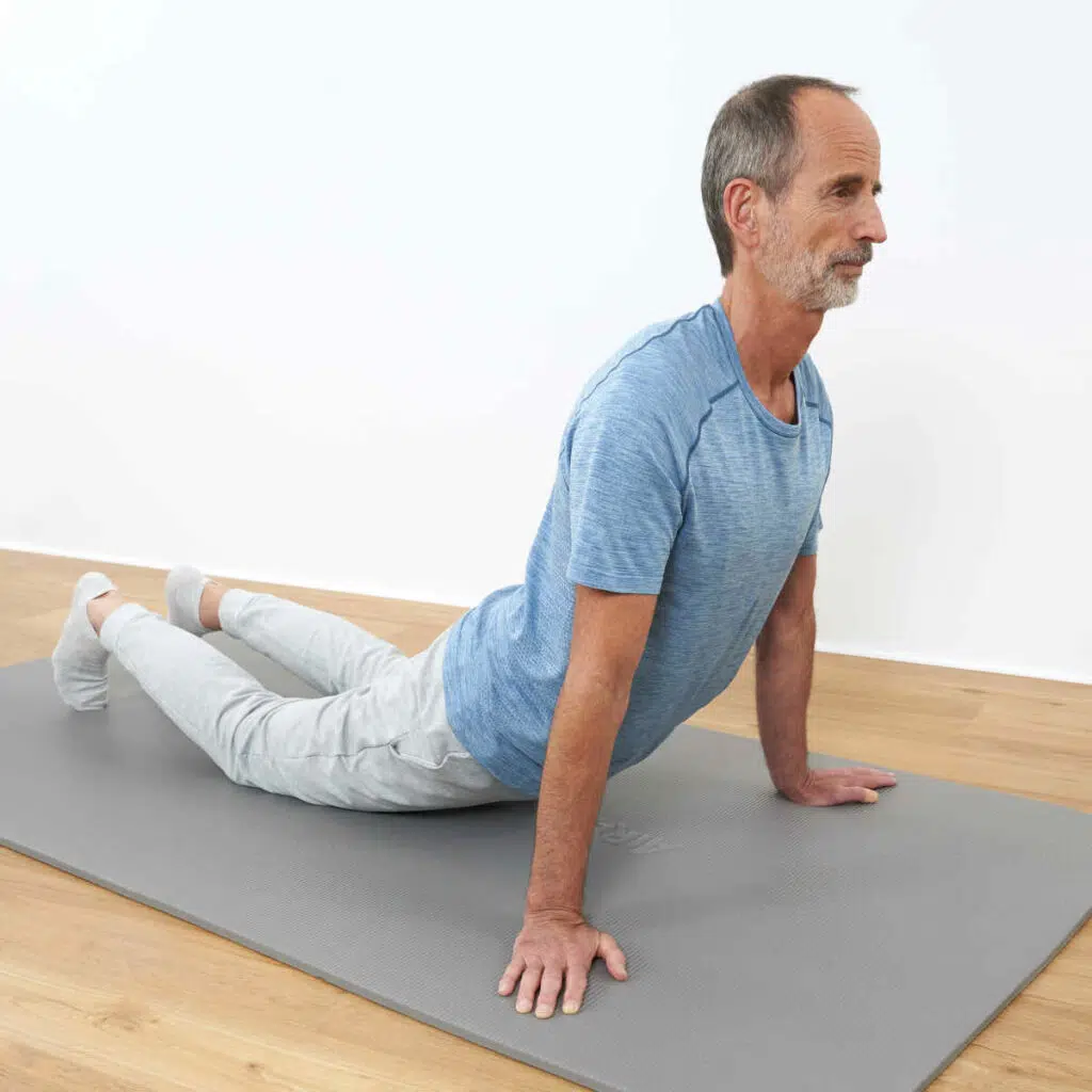 Roland Liebscher-Bracht führt auf einer Trainingsmatte eine Dehnübung aus. Er streckt die Beine nach hinten, seine Leiste ist am Boden und er stützt den Oberkörper mit seinen Armen hoch.