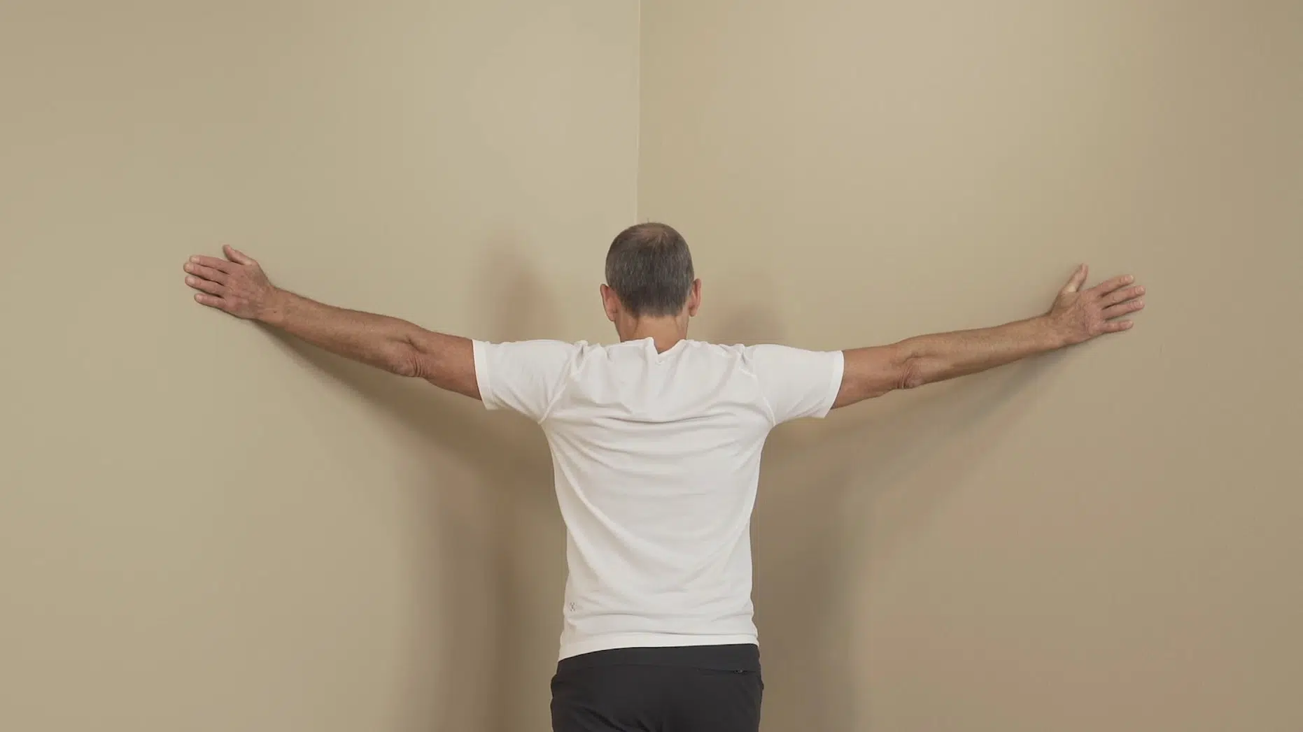 Eine Person steht in einer Zimmerecke und hat die Arme weit ausgebreitet. Sie lehnt sich in die Ecke hinein, um die Brustwirbelsäule zu dehnen.