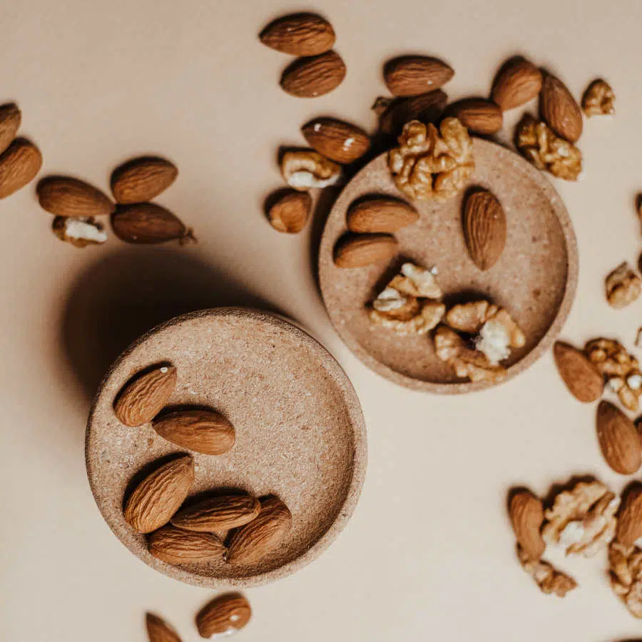 Mandeln und Walnüsse liegen auf zwei kleinen braunen Tellern verteilt. Auch um sie herum liegen die Nüsse auf dem Tisch.