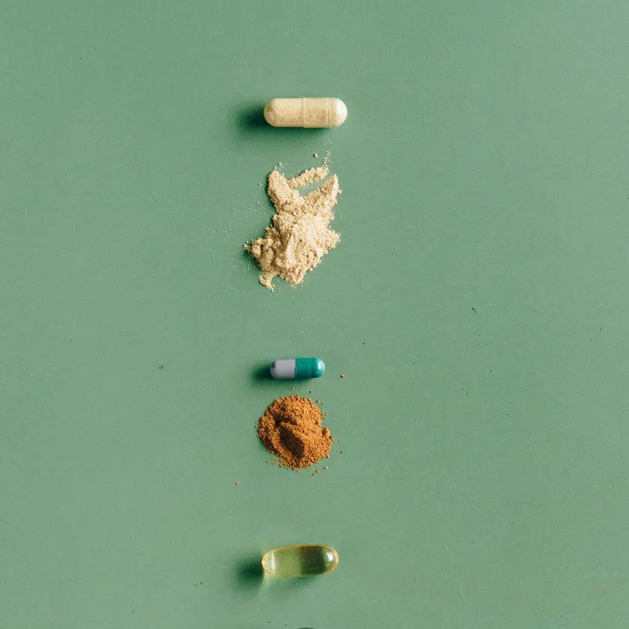 Auf einem grünen Untergrund liegen drei verschieden gefüllte Kapseln untereinander und dazwischen jeweils ein Wirkstoff in Pulverform.