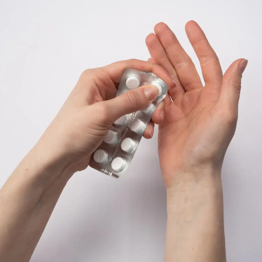 Die linke Hand einer Frau drückt eine weiße Pille aus einem Blister. Die rechte Hand hält sie unter den Blister, um die Pille aufzufangen.