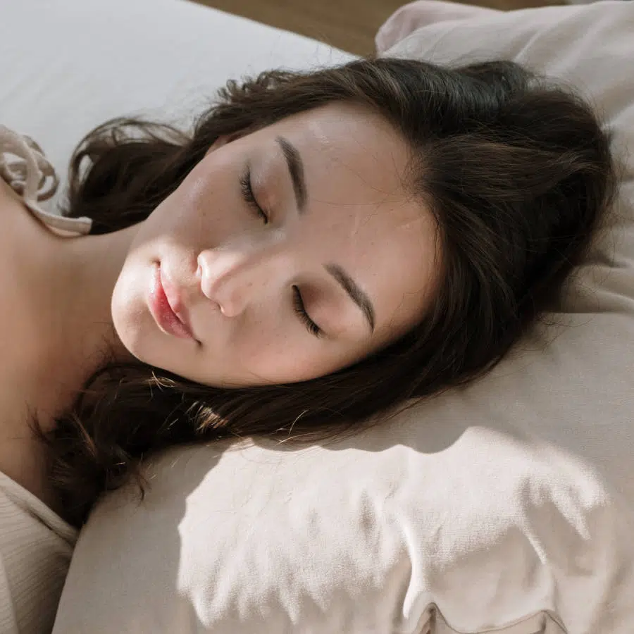 Eine junge Frau liegt im Bett auf ihrem Kopfkissen. Sie hat die Augen geschlossen und schläft.