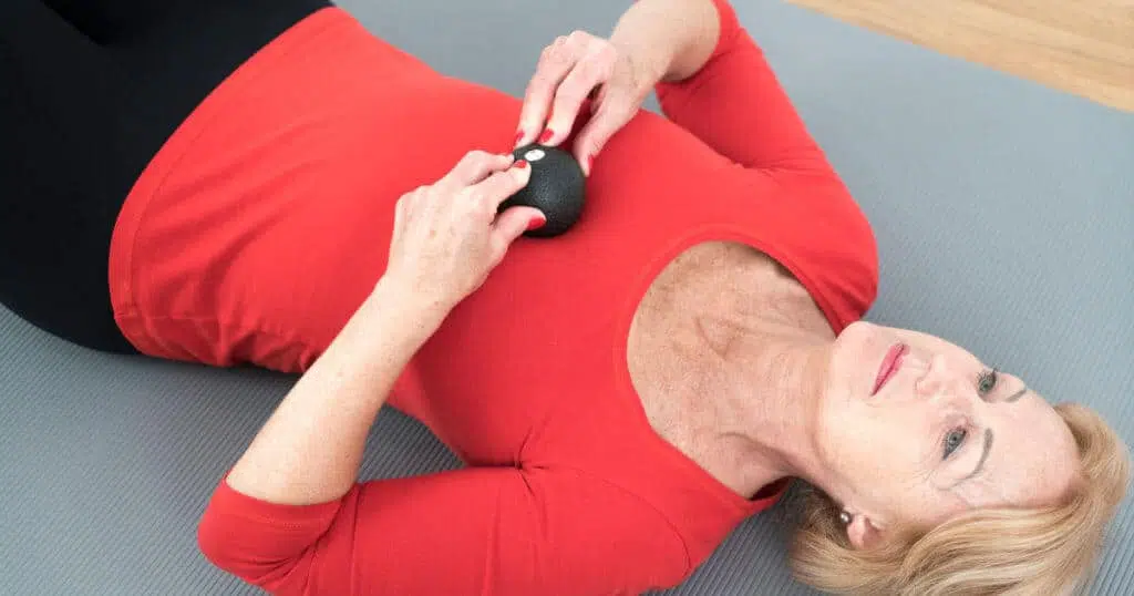 Eine Person liegt auf dem Rücken am Boden und hält mit beiden Händen die Mini-Kugel von Liebscher & Bracht. Die Mini-Kugel liegt auf ihrem Brustbein.