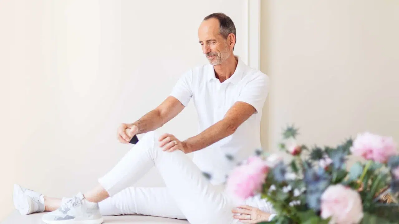 Schmerzspezialist Roland Liebscher-Bracht behandelt eine Patientin: Zu sehen sind ihre Beine, eines davon hat sie angewinkelt, sodass Roland Liebscher-Bracht mit der linken Hand ihr Knie festhalten kann und mit der anderen den Schmerzfrei-Drücker ansetzen kann.