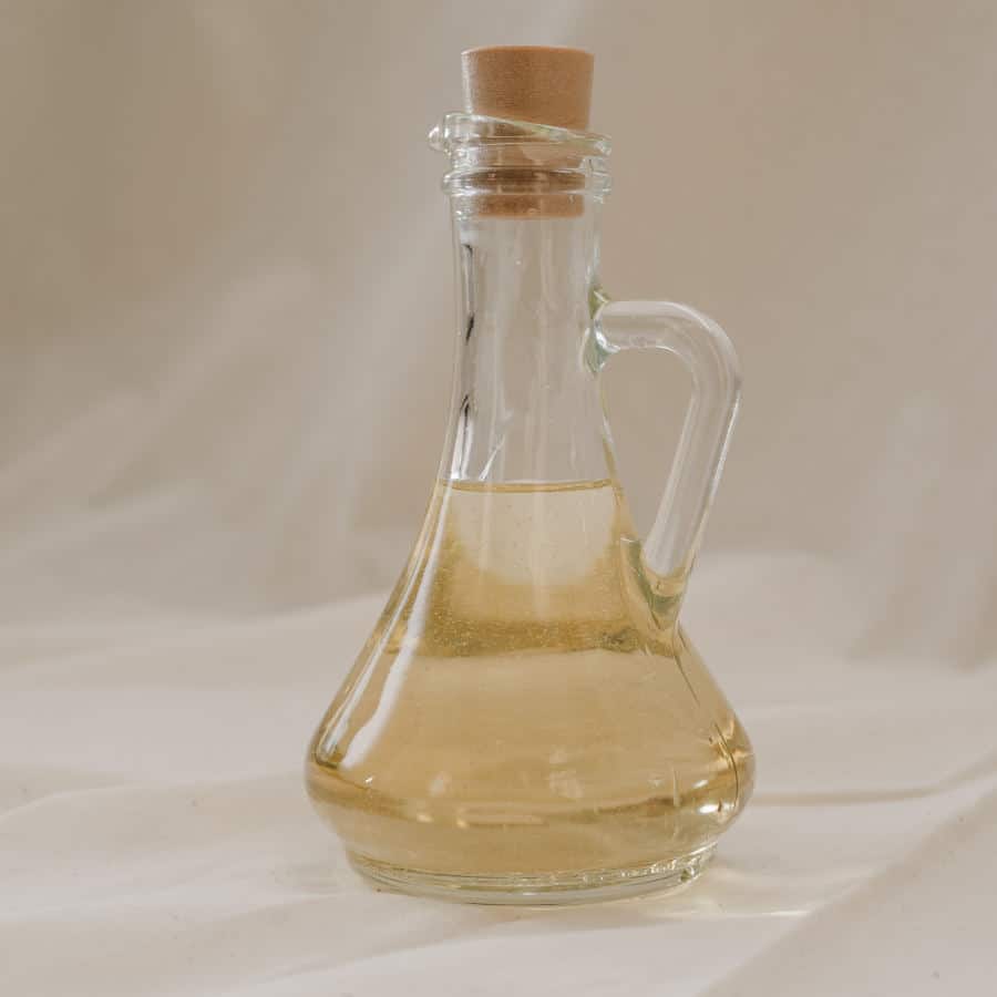 Ein hochwertiges, entzündungshemmendes gelbliches Pflanzenöl ist in einem gläsernen Krug mit Korkverschluss zu sehen.