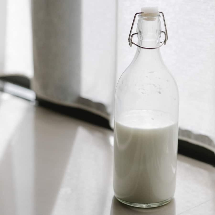 Frische Milch steht abgefüllt in einer Glasflasche auf dem Boden. Licht von außen fällt in den Raum und wird vom Boden reflektiert.