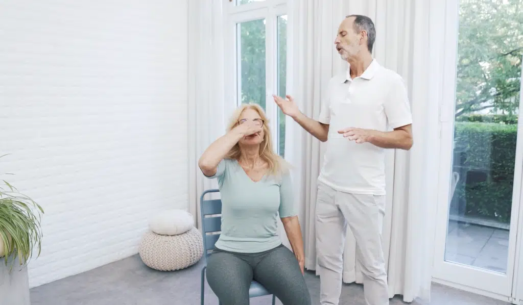 Eine Person sitzt auf einem Stuhl und hält sich die Nase zu, weil sie eine Atemübung durchführt.