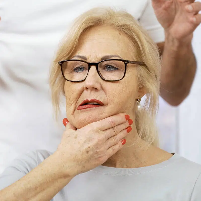 Eine Frau hat ihren Mund leicht geöffnet und schiebt ihren Unterkiefer zur rechten Seite. Mit ihrer rechten Hand unterstützt sie diese Bewegung.