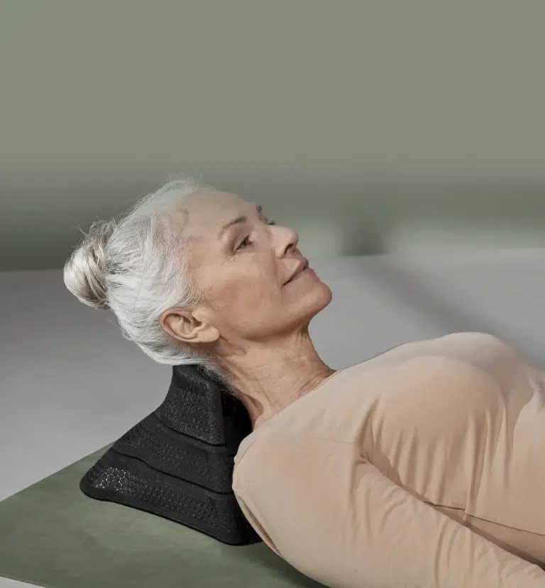 Eine ältere Frau liegt mit ihrem Hinterkopf auf dem Aufsatz des Liebscher & Brachts-Hilfsmittels, dem Nackenretter.