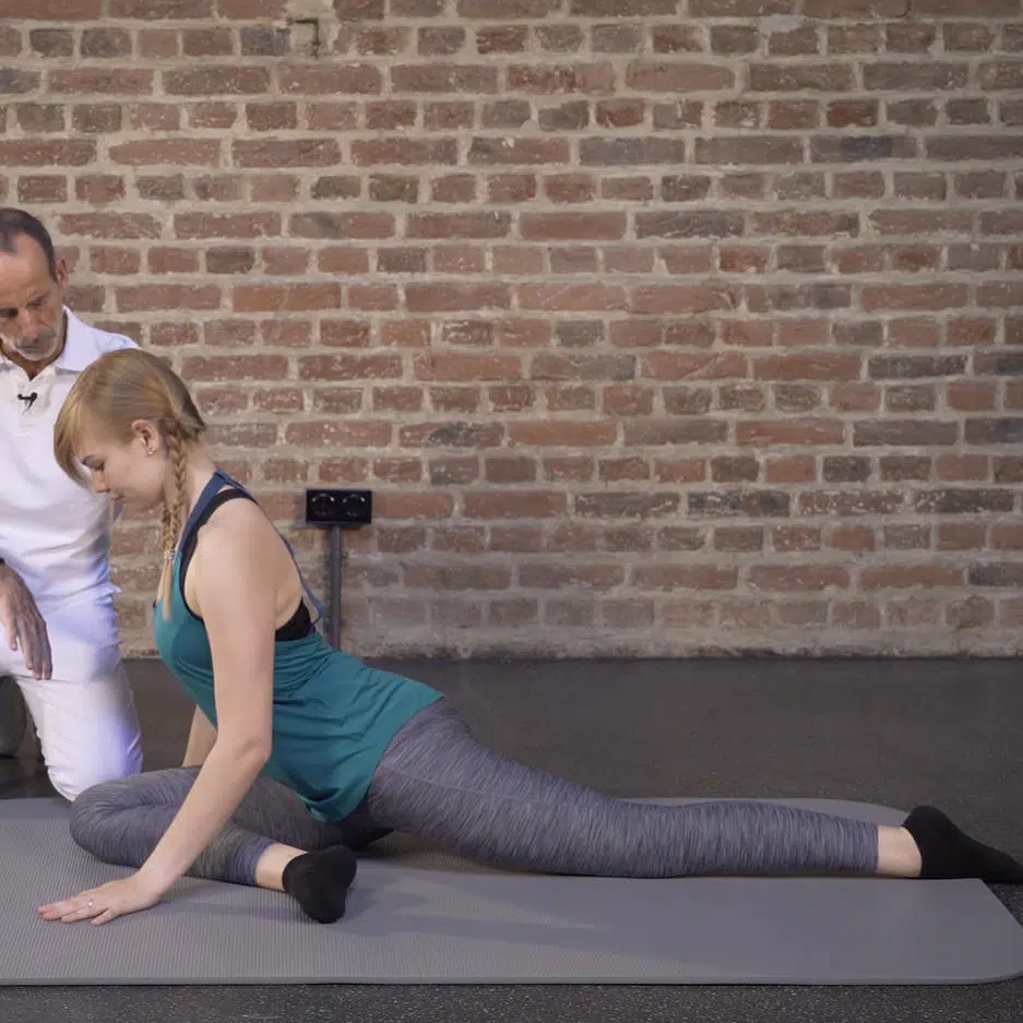 Eine junge Frau hat auf einer Übungsmatte ihr linkes Bein lange nach hinten ausgestreckt, während sie ihr rechtes Bein vorne anwinkelt.