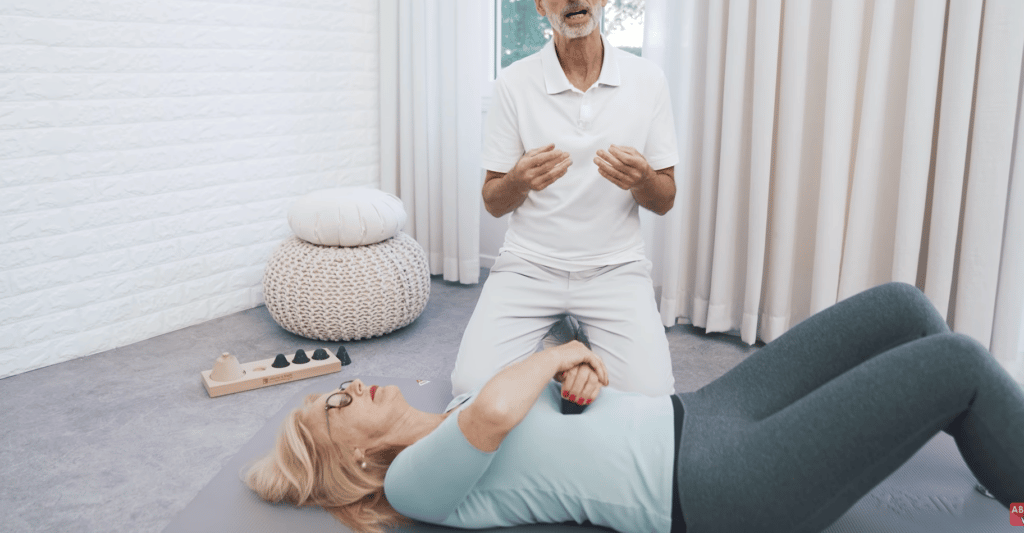 Eine Person liegt auf dem Rücken auf dem Boden und hält den Drücker in der Hand. Damit drückt sie ihr Brustbein, um die Muskulatur im Brustkorb zu lockern.