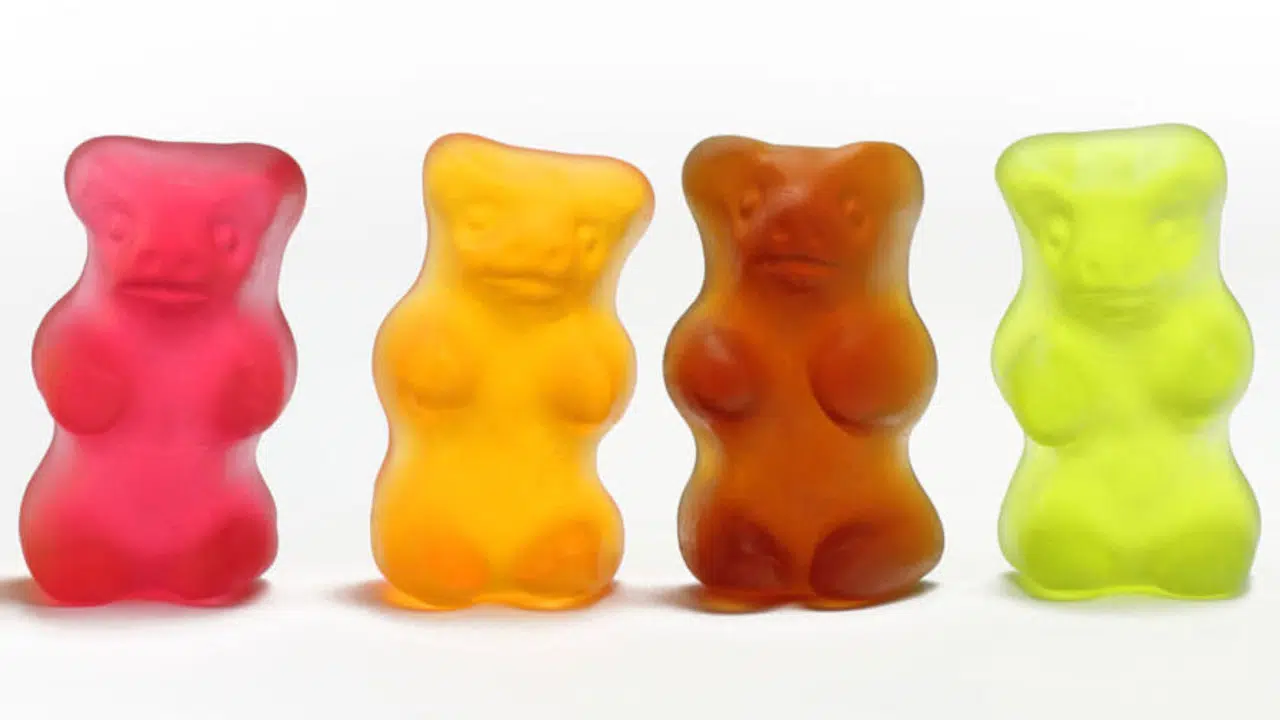 Vier Gummibärchen in gelb, rot, orange, rot-braun und grün stehen in einer Reihe nebeneinander.