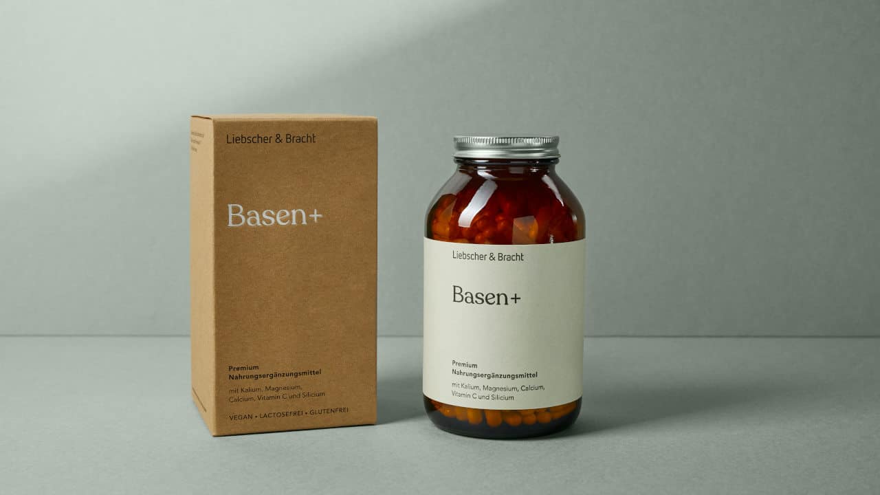 Eine Braunglasflasche und ein Faltkarton jeweils mit der Beschriftung Basen Plus stehen vor einem grünen Hintergrund.