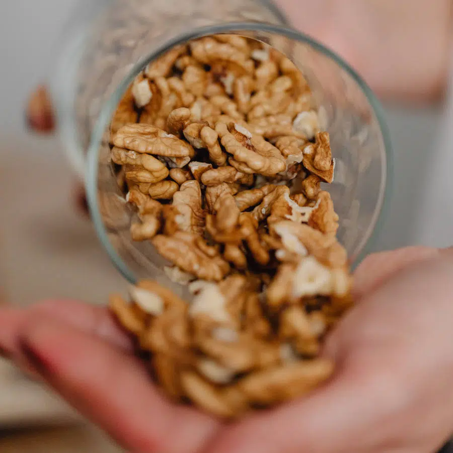 Eine Hand hält ein Glas mit Walnüssen und schüttet einige Walnüsse in die andere offene Hand vor dem Glas.