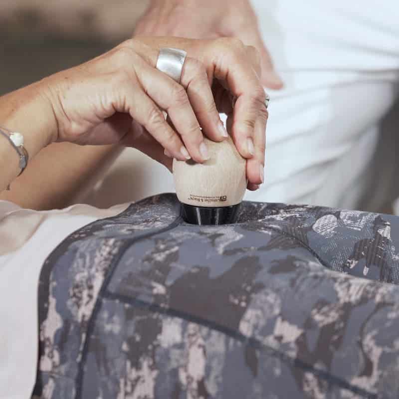 Eine Frau hält in beiden Händen den Schmerzfrei-Drücker von Liebscher und Bracht und setzt ihn mit der Spitze an ihrem Beckenknochen an.