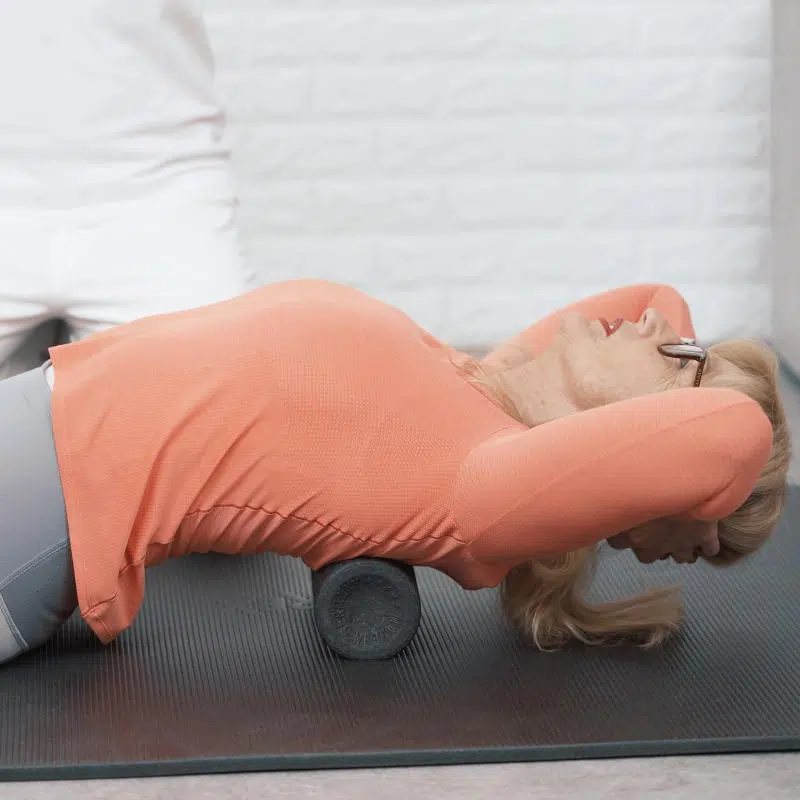 Eine Frau liegt am Boden mit ihrem oberen Rücken auf einer Faszienrolle.