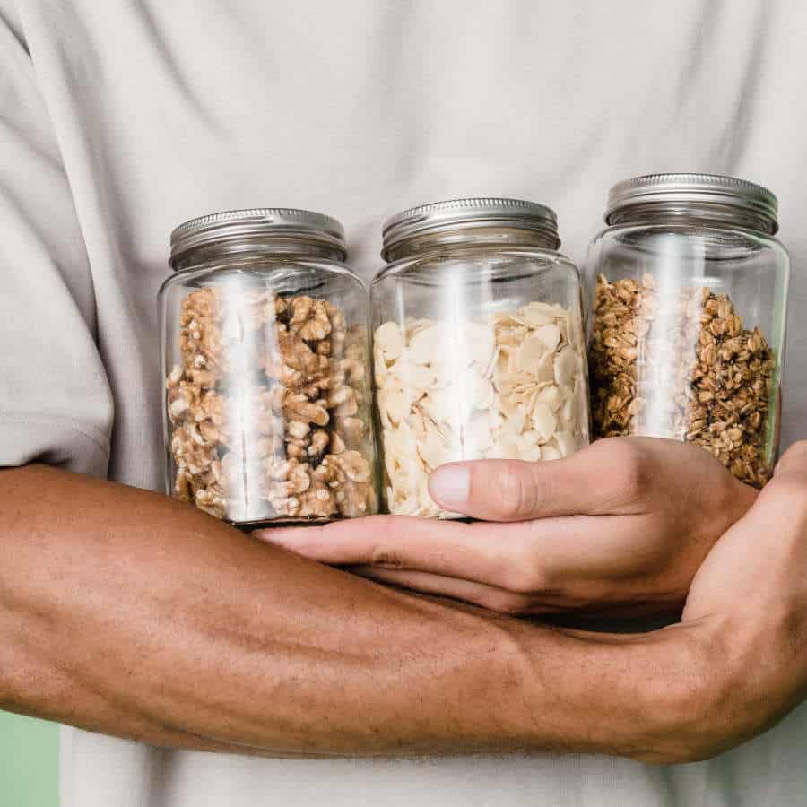 Ein Mann hält drei Vorratsgläser mit verschiedenen Nüssen vor seinen Körper.