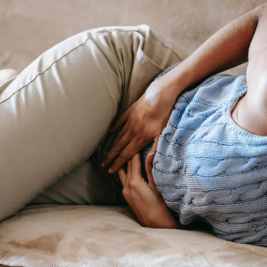 Eine Frau liegt seitlich auf einem Sofa und hält sich mit beiden Händen den Bauch.