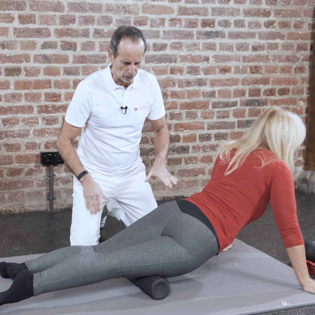 Eine Frau liegt mit ihrem rechten Oberschenkel auf einer Faszienrolle. Mit ihren Armen hebt sie ihren Oberkörper ab, um auf der Faszienrolle nach unten rollen zu können.