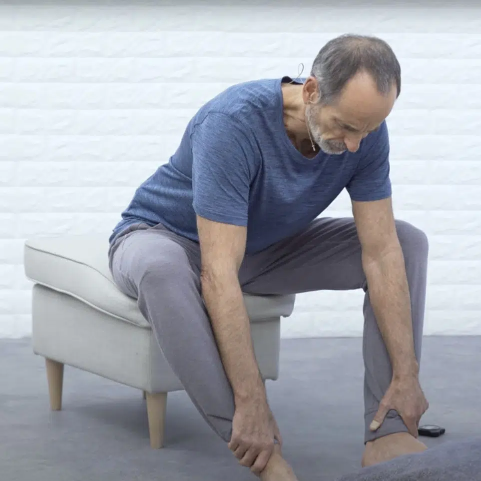 Eine Person sitzt auf einem Hocken und beugt sich nach vorne. Sie greift ihre Knöchel und zieht sich nach vorne und unten.