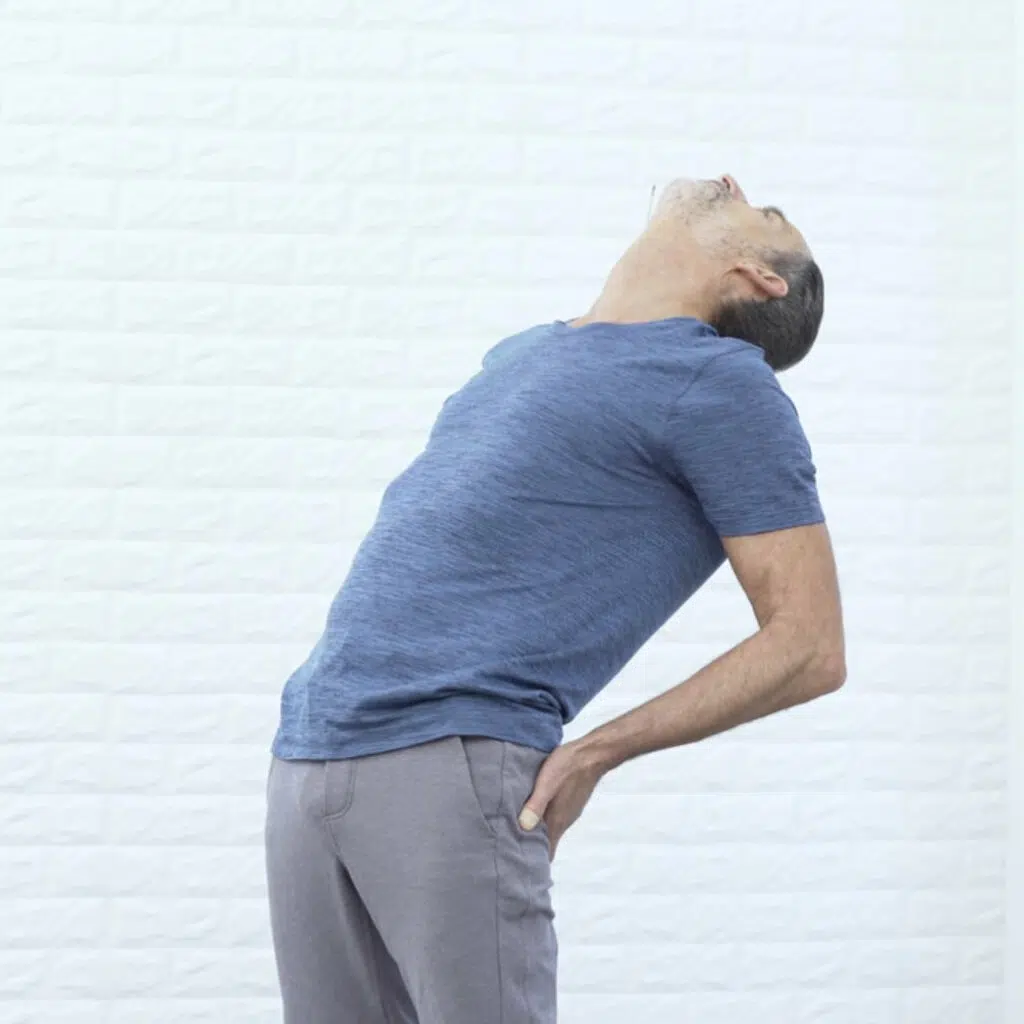 Eine Person hat im Stehen beide Hände auf das Gesäß abgelegt und lehnt sich weit nach hinten. Die Hüfte schiebt nach vorne, der Kopf hängt nach hinten.