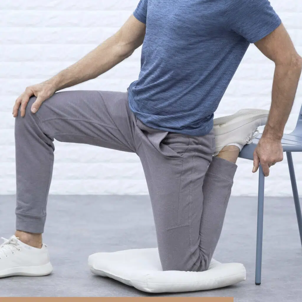 Roland Liebscher-Bracht hat sein linkes Bein vor einem Stuhl senkrecht angewinkelt. Dabei liegt sein Fuß auf der Stuhlfläche. Sein rechtes Bein ist aufgestellt.