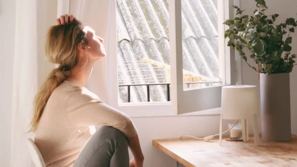 Eine junge Frau sitzt am offenen Fenster und die Sonne scheint auf ihr Gesicht.