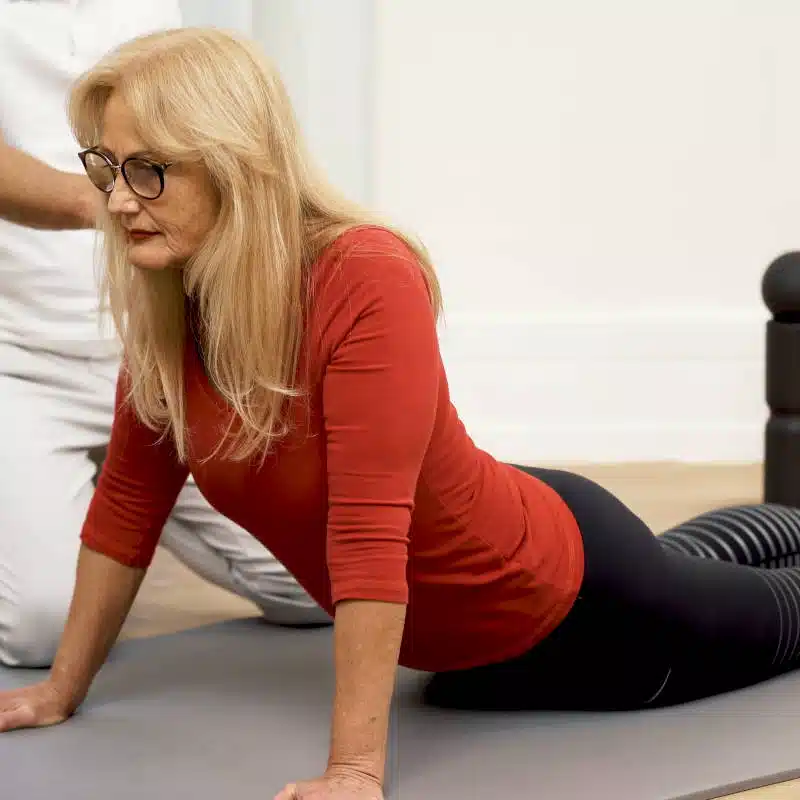 Eine Frau liegt auf einer Yoga-Matte und hat ihren Oberkörper mit ausgestreckten Armen vom Boden weggedrückt.