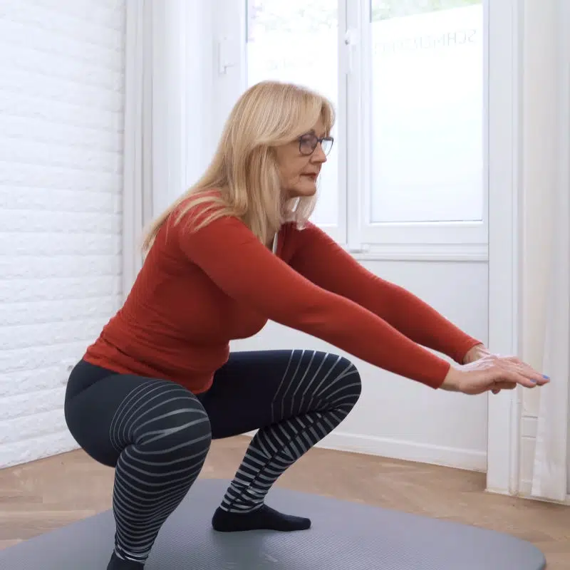 Eine Frau macht eine tiefe Kniebeuge. Ihre Beine stehen dabei weit auseinander.