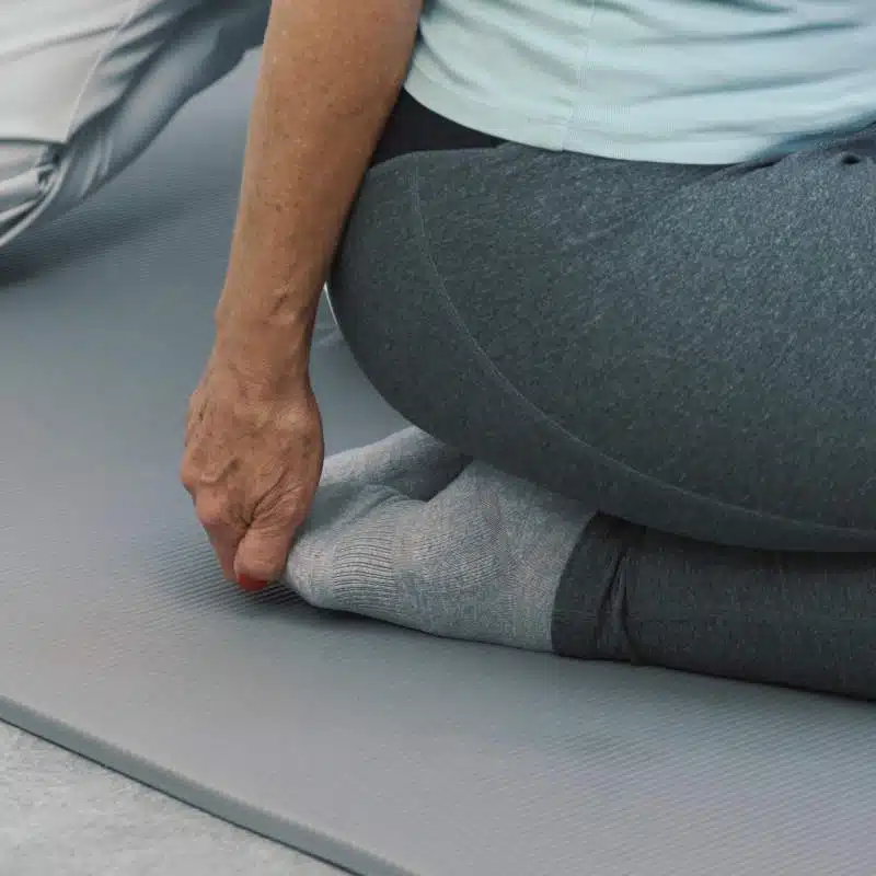 Eine Person sitzt mit dem Gesäß auf ihren Fersen und zieht mit einer Hand die Zehen nach oben.