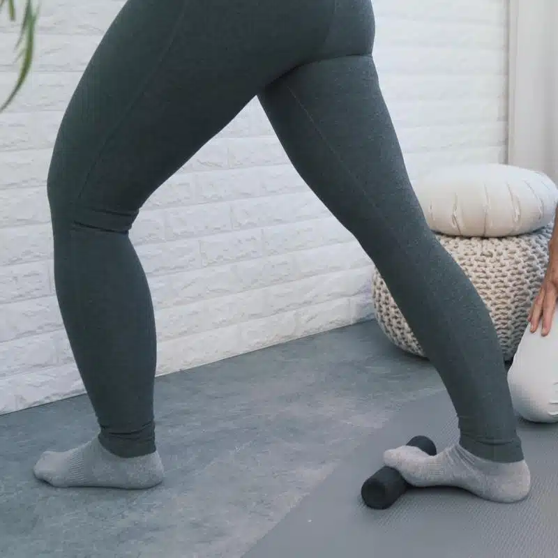 Eine Person hat einen Ausfallschritt gemacht und steht mit den Zehen des hinteren Fußes auf einer kleinen Faszienrolle.