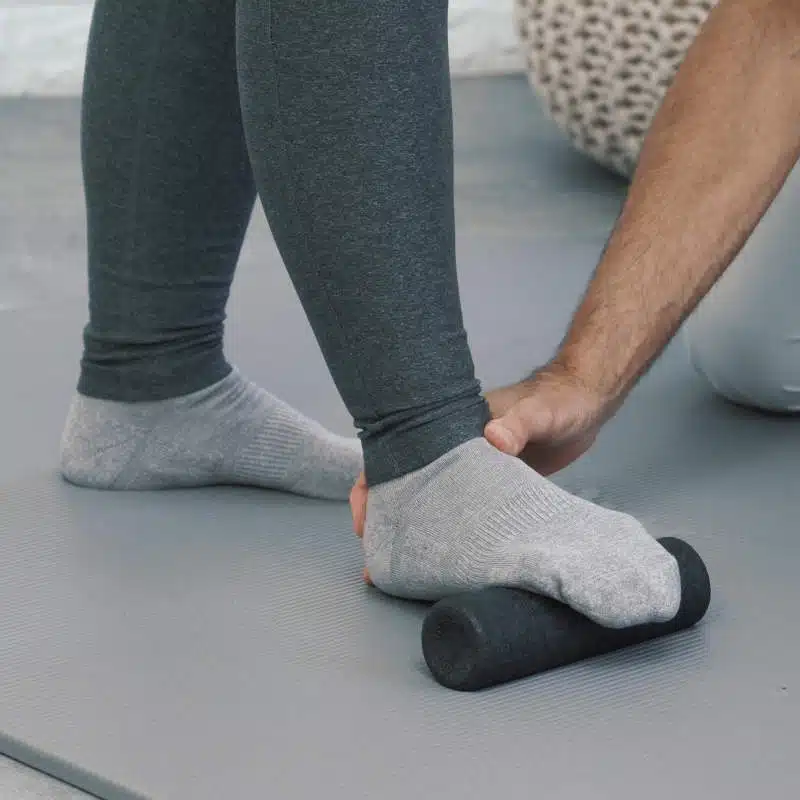 Eine Person hat ihren Vorfuß auf einer kleinen Faszienrolle platziert und die Zehen nach unten gebeugt.