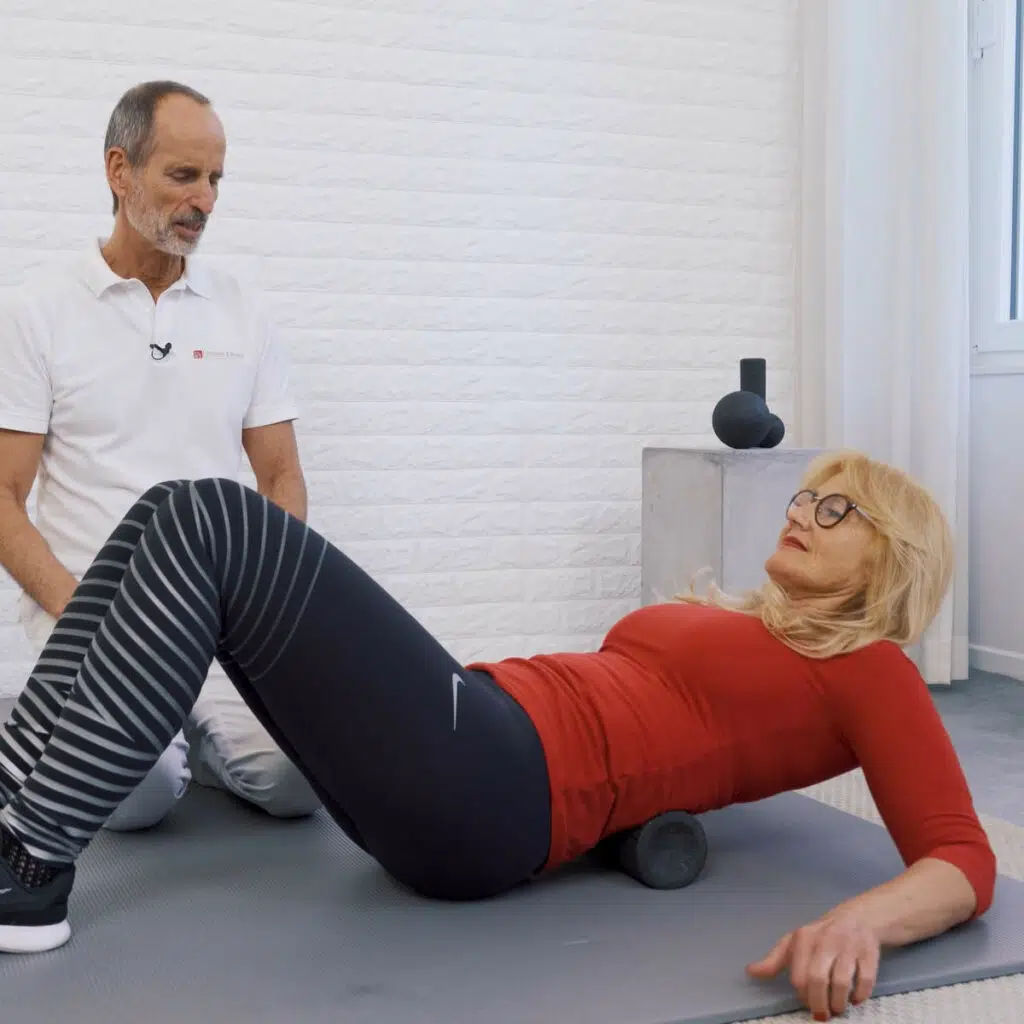 Eine Frau liegt ihrem Oberkörper auf der Medi-Faszienrolle von Liebscher & Bracht. Sie rollt nach unten, sodass die Faszienrolle ihren Rücken massiert.