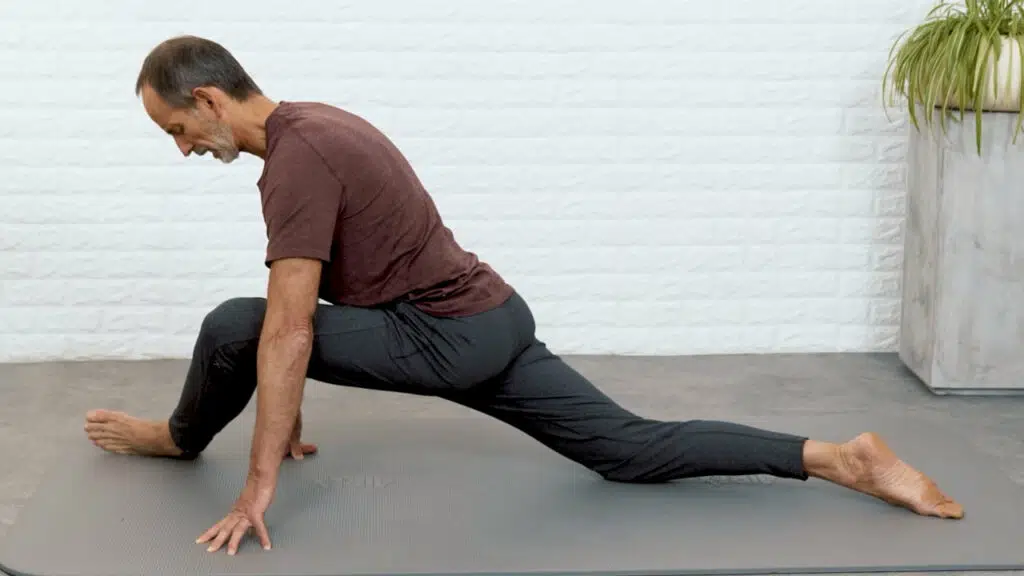 Roland Liebscher Bracht stützt sich mit beiden Händen vom Boden ab. Sein linkes Bein ist nach vorne angewinkelt, sein rechtes Bein nach hinten ausgestreckt. Das Becken schwebt etwa 30 Zentimeter über der Matte und ist horizontal ausgerichtet.