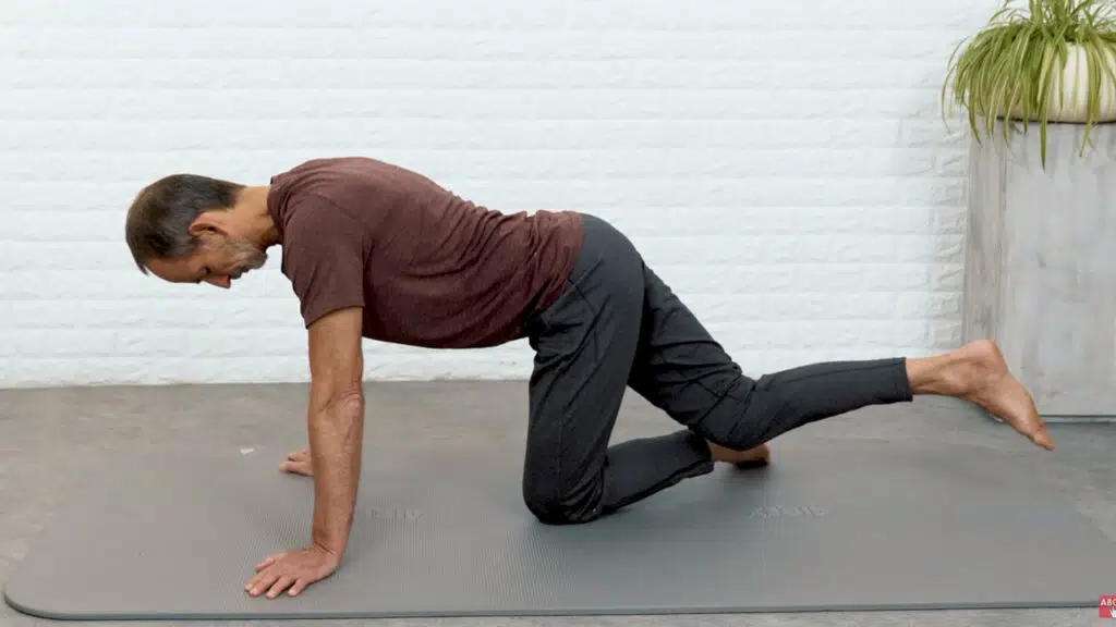 Roland Liebscher-Bracht ist im Vierfüßlerstand und hat das rechte Bein leicht angehoben, sodass er hinten nur auf dem linken Knie steht.