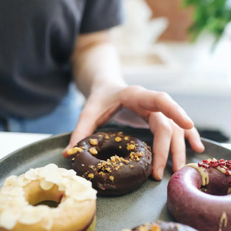 Mehrere Donuts liegen auf einem Teller. Eine Hand greift nach einem Schoko-Donut.