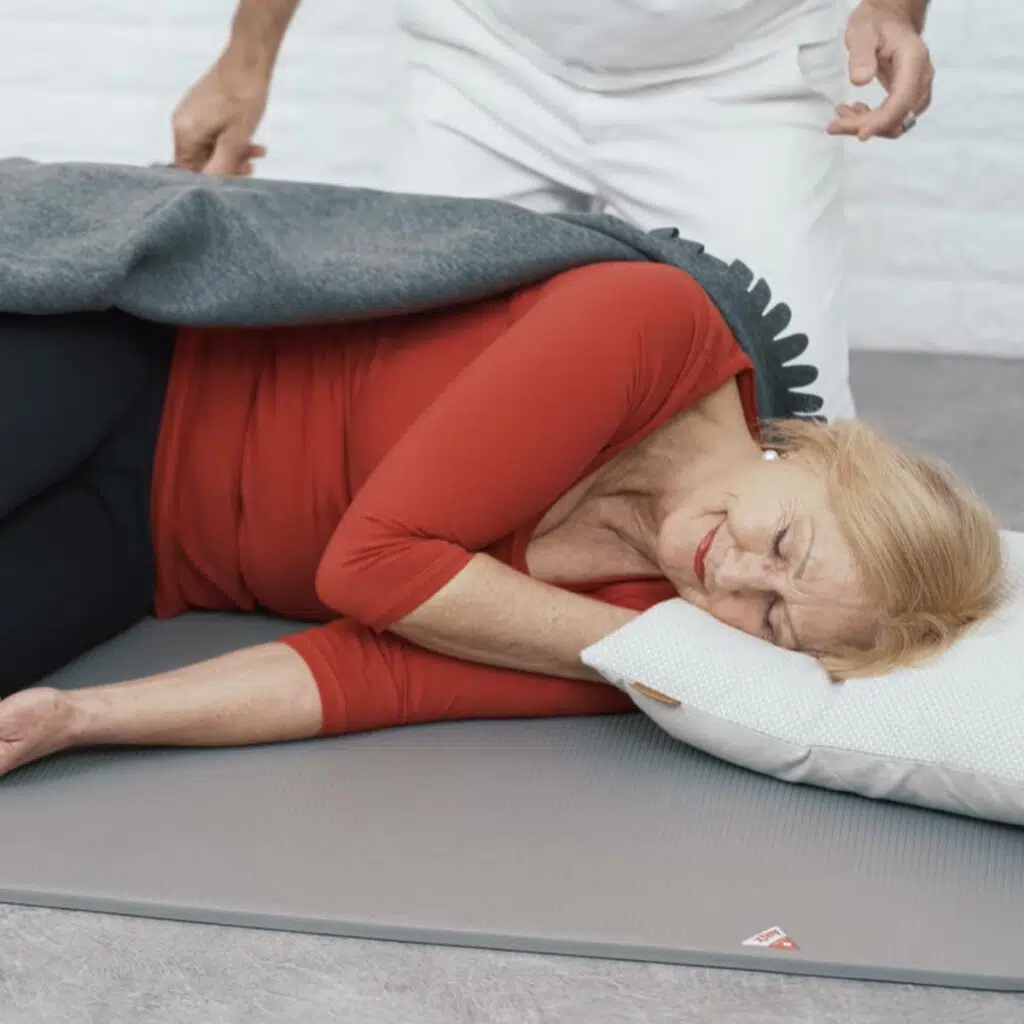 Eine Frau liegt auf der Seite. Die Beine hat sie angewinkelt, eine Hand liegt unter dem Kopfkissen.