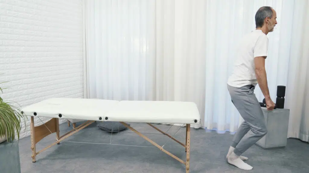 Roland Liebscher-Bracht steht am Ende einer therapeutischen Liege und richtet sich langsam auf.