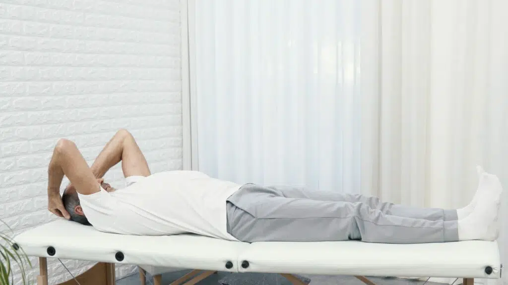 Roland Liebscher-Bracht liegt auf einer therapeutischen Liege, seine Beine sind lang ausgestreckt. Seine Arme liegen an seinem Hinterkopf.