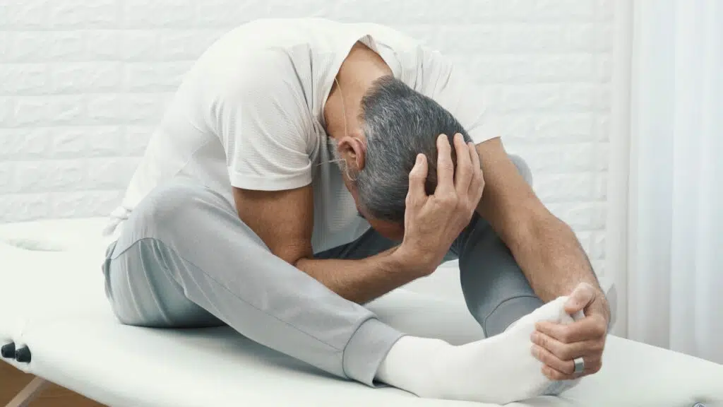 Roland Liebscher-Bracht sitzt auf einer therapeutischen Liege. Die Beine sind leicht angewinkelt. Er rundet seinen Rücken und zieht sich mit einer Hand an seinen Füßen nach vorne. Die zweite Hand an seinem Hinterkopf führt sein Kinn zur Brust.