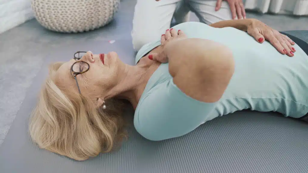 Die Patientin liegt auf dem Rücken auf eine Matte. Sie hat eine Hand auf den Brustkorb abgelegt, die andere Hand liegt auf dem Bauch.