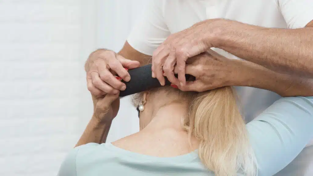 Die Patientin hält mit beiden Händen die Mini-Rolle fest und setzt sie schräg hinter dem linken Ohr an. Den Kopf neigt sie nach rechts unten.