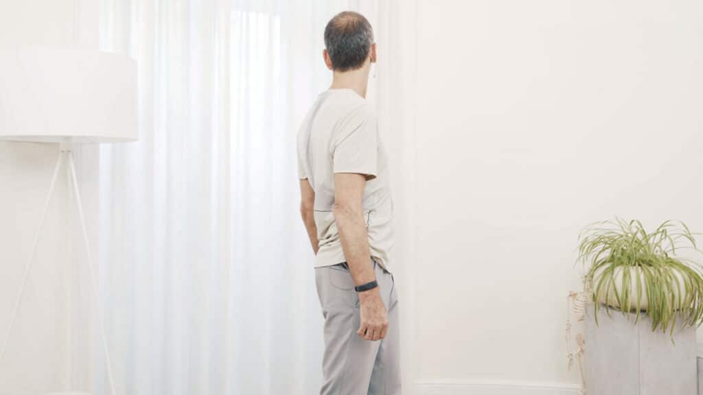 Roland Liebscher-Bracht steht gerade und rotiert die Wirbelsäule nach links und schaut über seine Schulter.