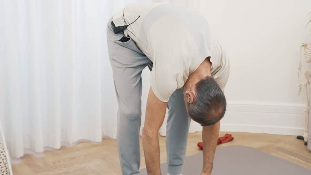 Roland Liebscher-Bracht macht eine Vorbeuge im Stehen. Er hat die Knie gebeugt und lässt seinen Oberkörper locker nach unten hängen.