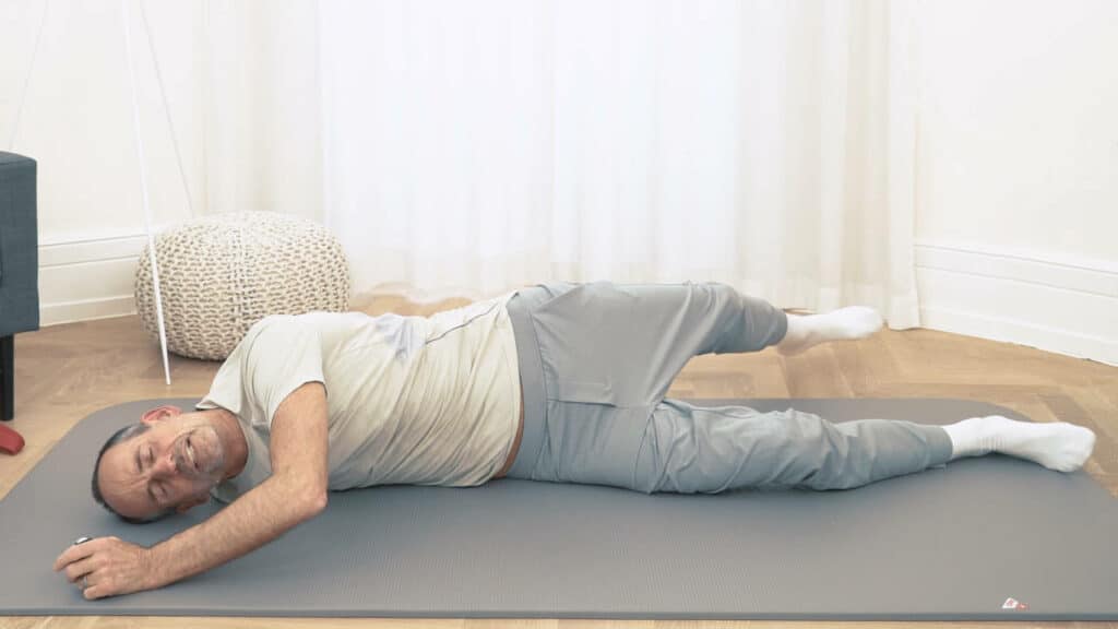 Roland Liebscher-Bracht liegt seitlich auf dem Boden und dreht seinen Oberkörper mithilfe des linken Arms.