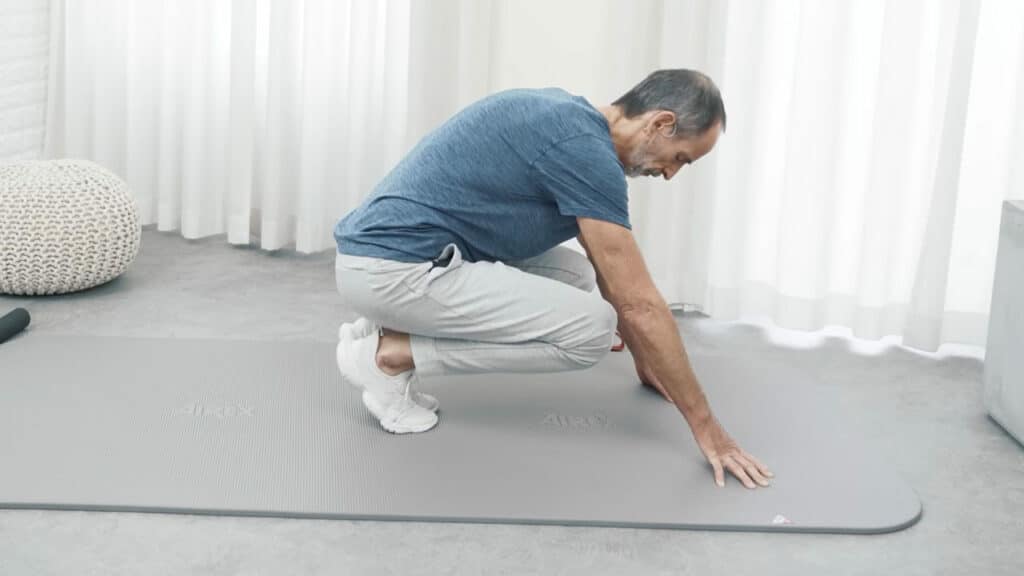 Roland Liebscher-Bracht befindet sich in einer hockenden Position auf der Übungsmatte.