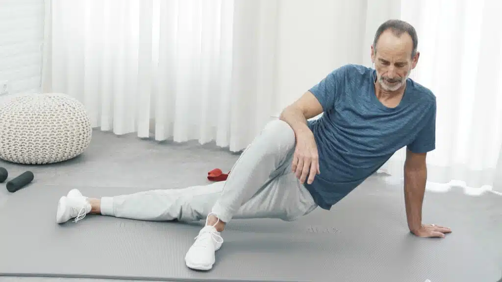 Roland Liebscher-Bracht befindet sich auf der Übungsmatte in einer seitlichen Position: Er stemmt sich mit der linken Hand hoch und lässt dabei seine linke Körperseite durchhängen.
